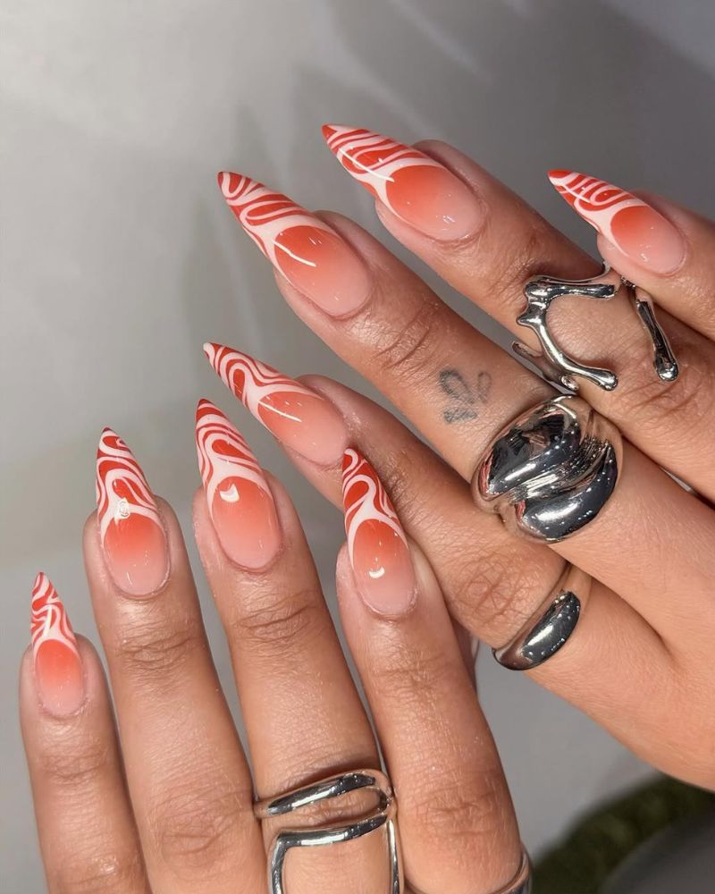 long stiletto nails with orange ombre french tip and swirly nail art design