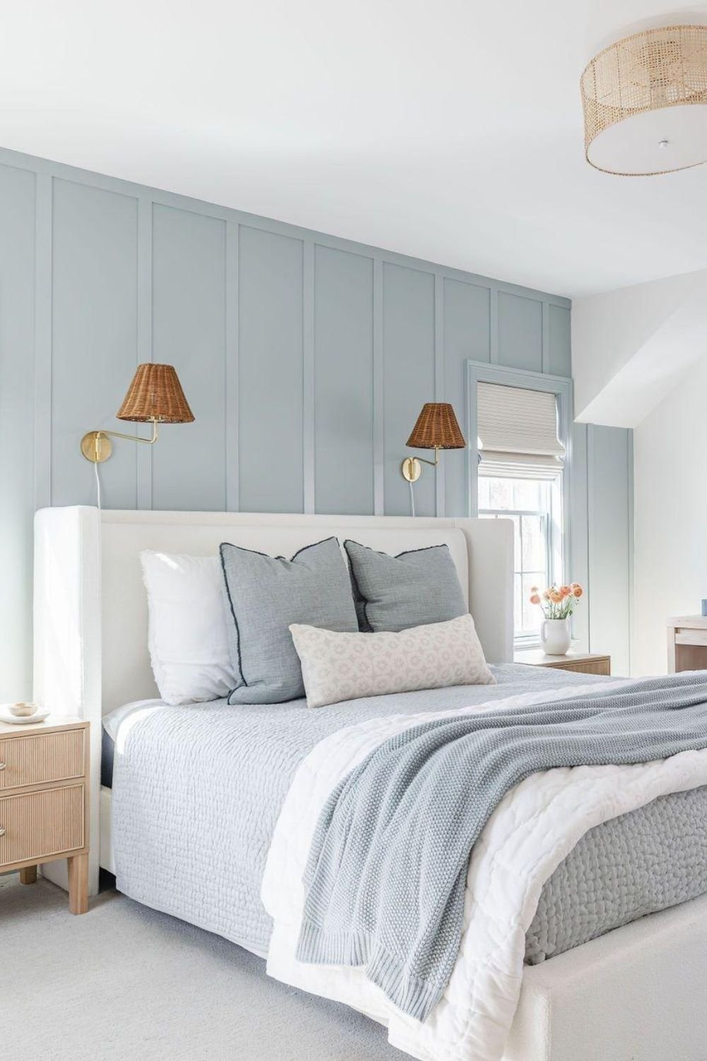 Muted blue vertical trim behind an upholstered bed with woven shades