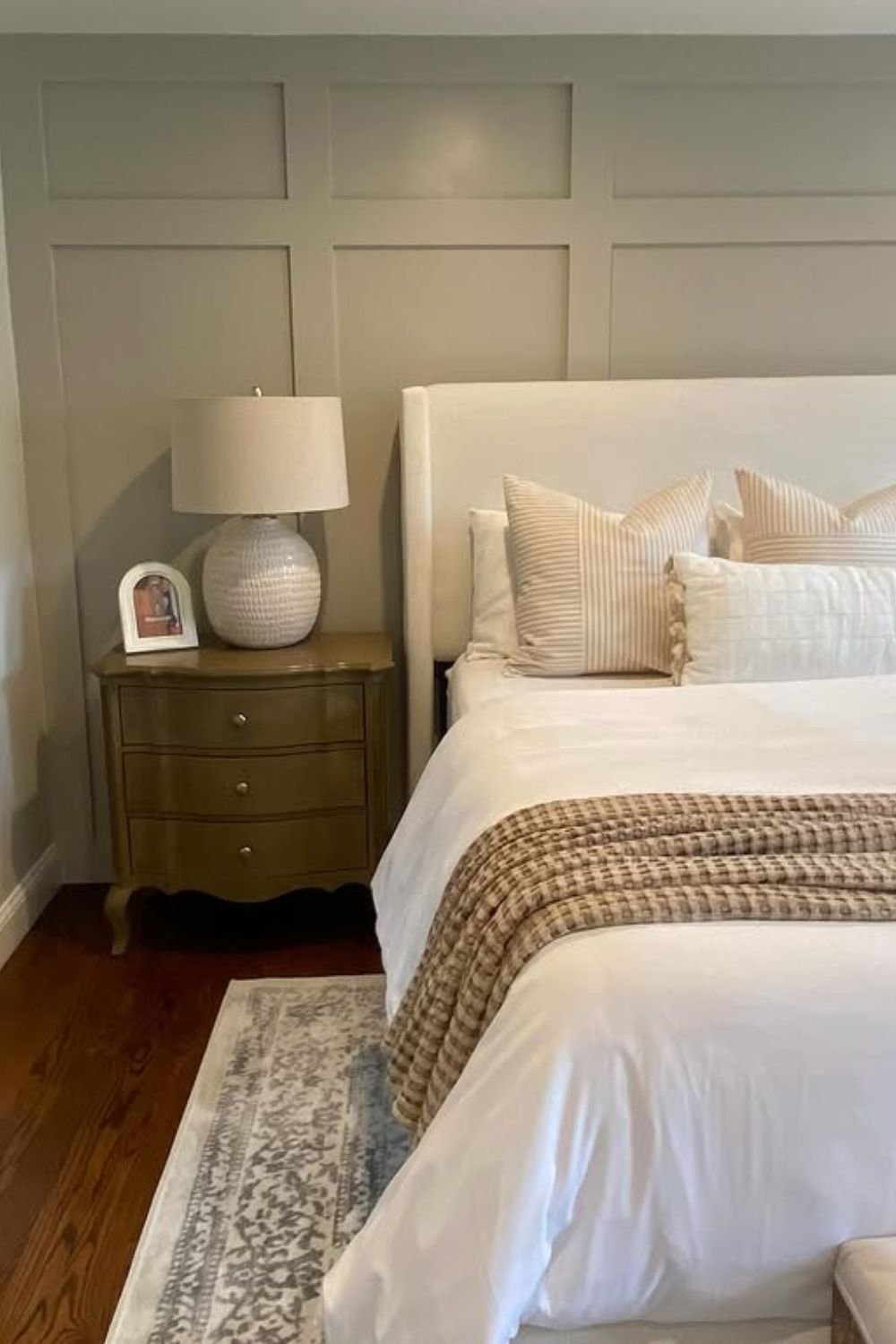 Greige grid wall behind an upholstered headboard with neutral bedding