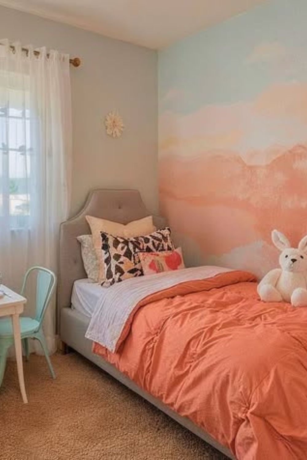 Cloud-like pastel mural behind a bed in blush, peach and sky blue tones