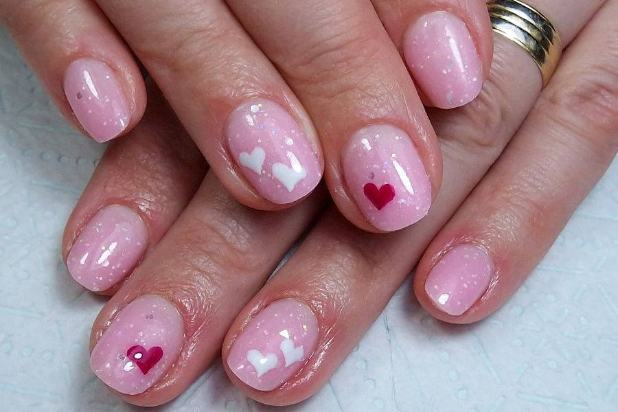 Baby pink square nails decorated with tiny white heart accents for a cute, romantic look.