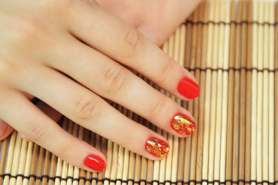 Bright orange square nails highlighted with shimmering gold leaf accent designs.