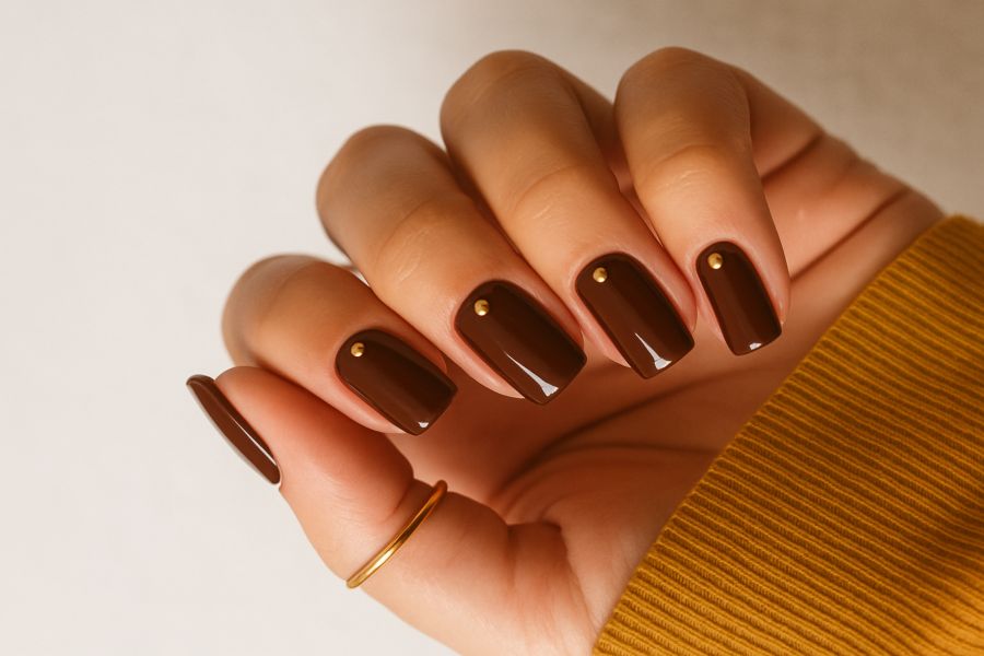 Chocolate brown square nails accented with small gold studs for a chic, minimalist style.