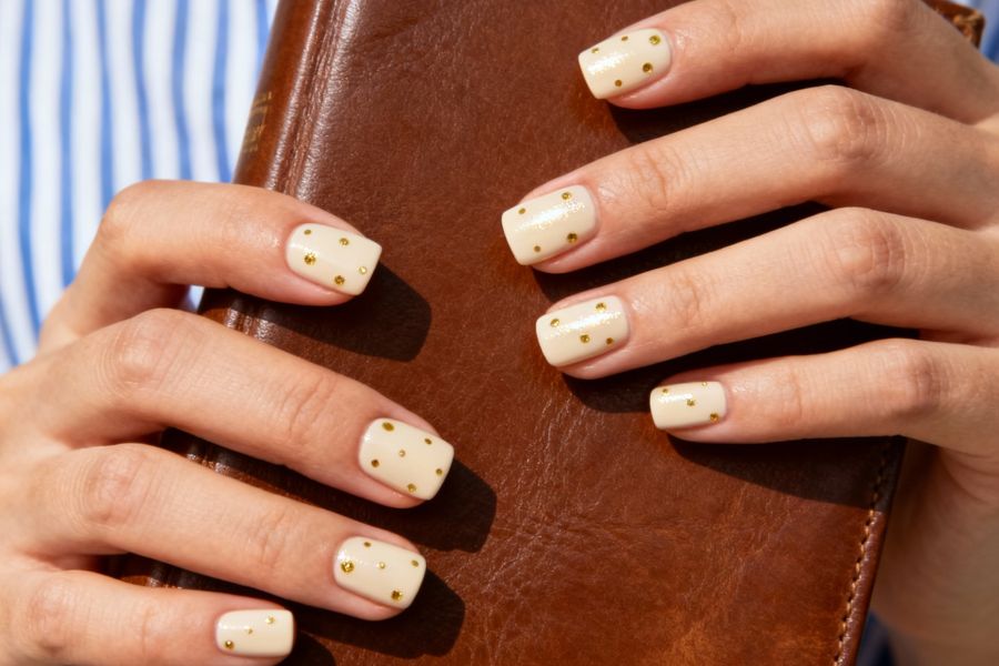 Cream square nails adorned with tiny gold dots for a simple yet elegant design.