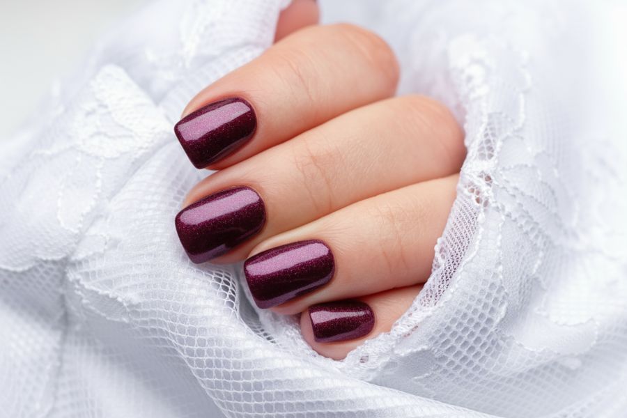 Close-up of deep burgundy square nails with a soft shimmer finish against a white lace fabric.