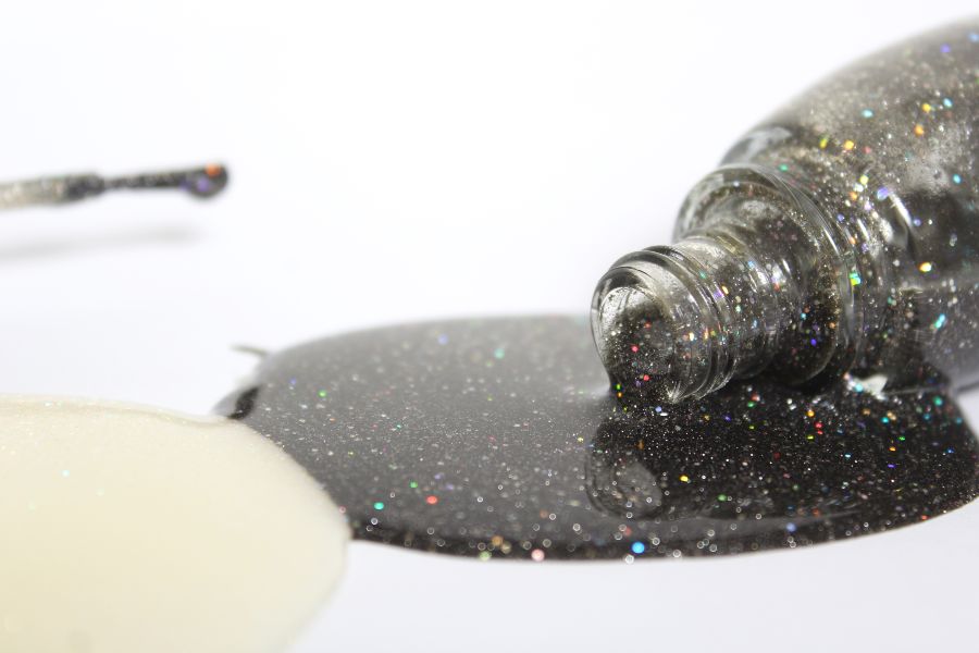Close-up of spilled holographic black nail polish with shimmering rainbow glitter.