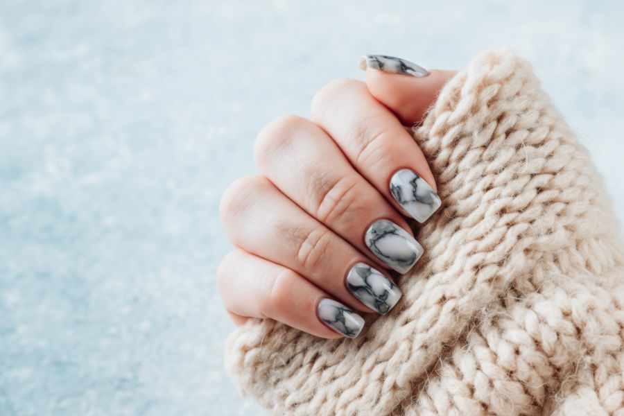 Close-up of grey and white marble effect square nails, hand wrapped in a beige knitted sweater.