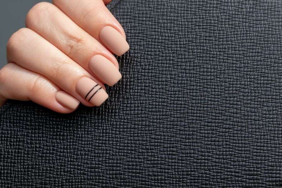 Close-up of matte beige square nails with minimalist thin black stripe accents on one finger.