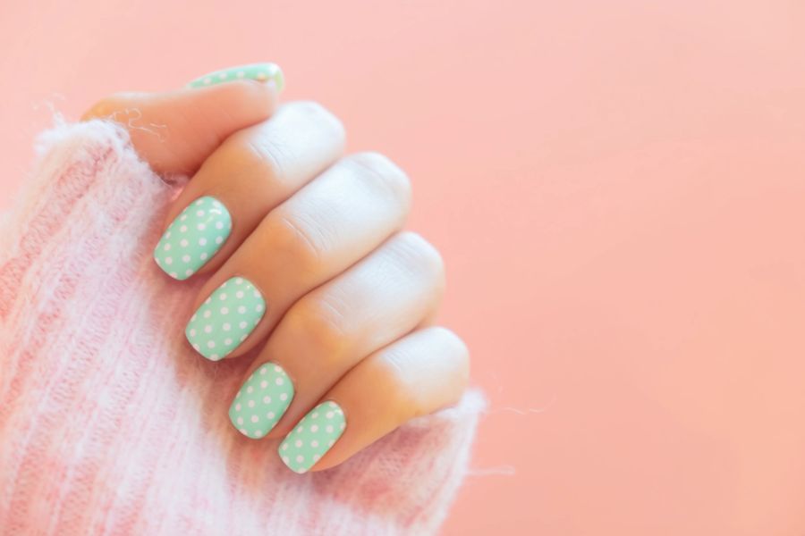 Mint green nails with white polka dots and a soft pink sweater background.