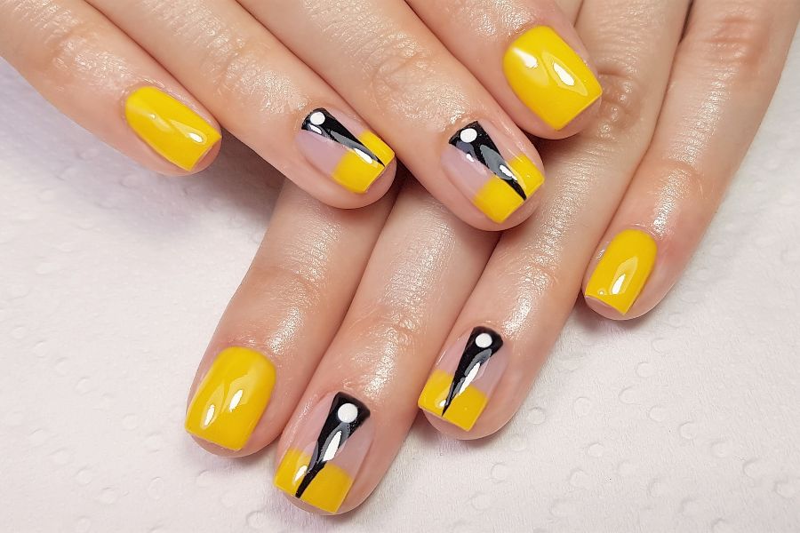 Mustard yellow nails with black, white, and lilac abstract geometric design accents.