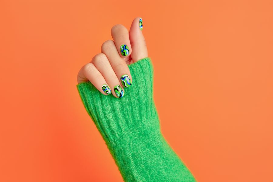 Hand with neon green square nails featuring bold abstract squiggle art against an orange background.