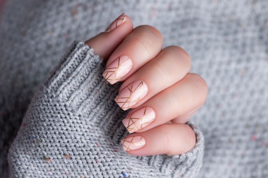 Pale peach square nails adorned with fine gold geometric line designs for a modern, elegant style.