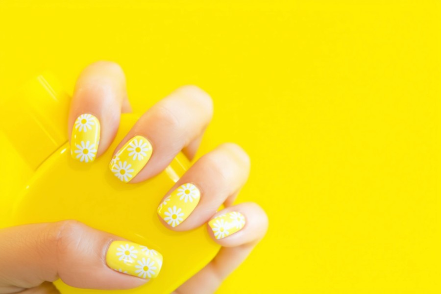 Glossy pale yellow square nails adorned with white daisy flower designs for a cheerful spring look.