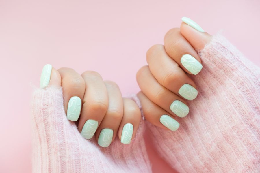 Pastel green square nails decorated with soft white swirl designs for a fresh, playful look.