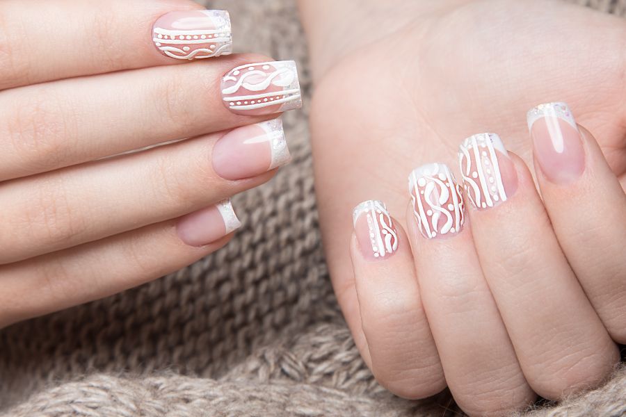 White patterned French manicure with glossy nude base and elegant swirl designs.