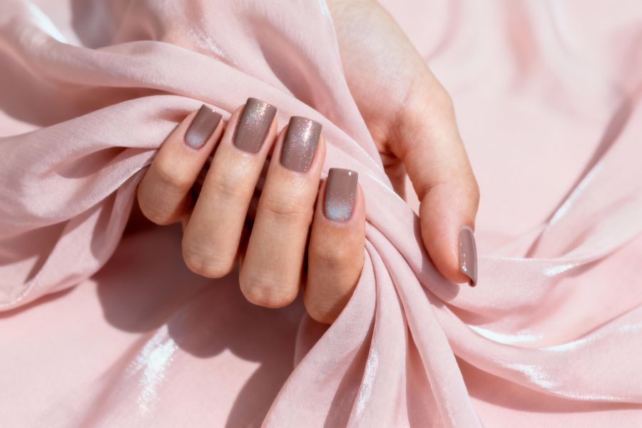 Taupe square nails with a soft glitter gradient against a pink fabric background.