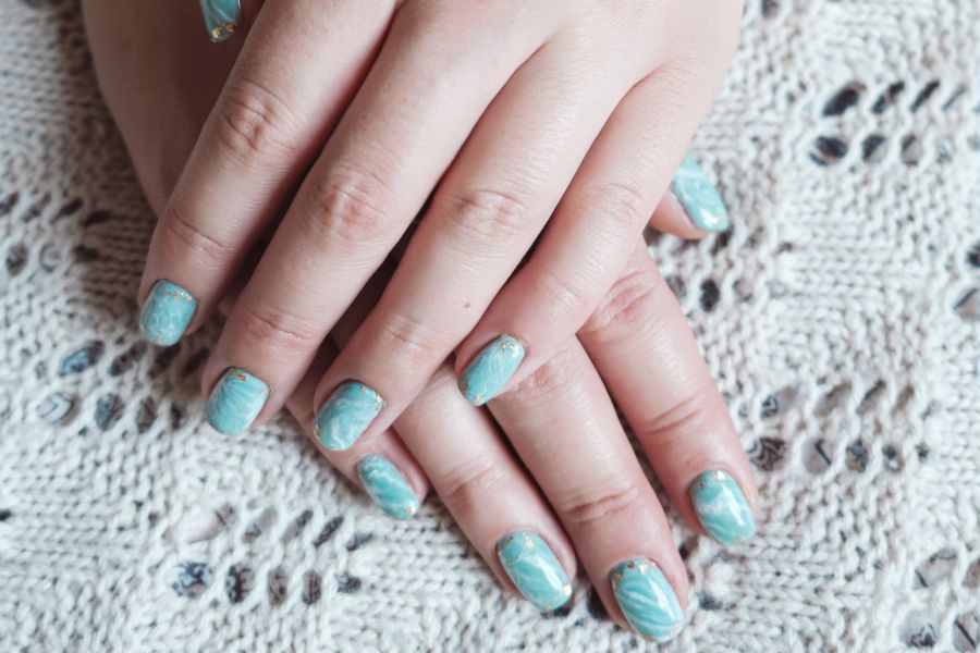 Teal square nails featuring a white marble effect and gold embellishments for a refined look.