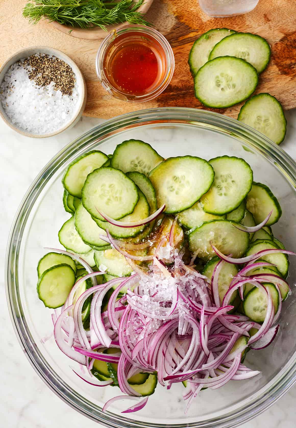 Thinly sliced cucumbers and red onion in glass mixing bowl