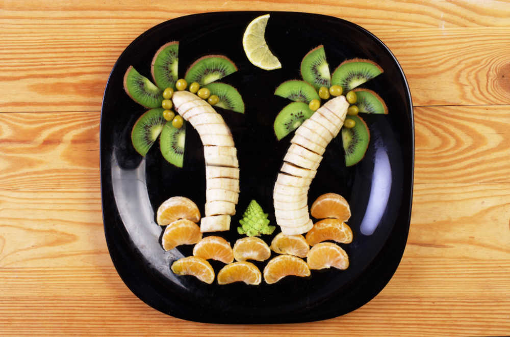 Banana carving scene: Bananas, kiwi fruit and oranges in a palm tree scene.