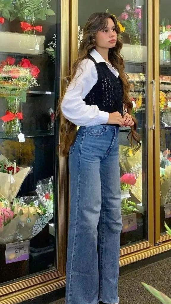 Fashion-forward fall outfit featuring white blouse, black vest, and wide-leg jeans in front of flower shop.