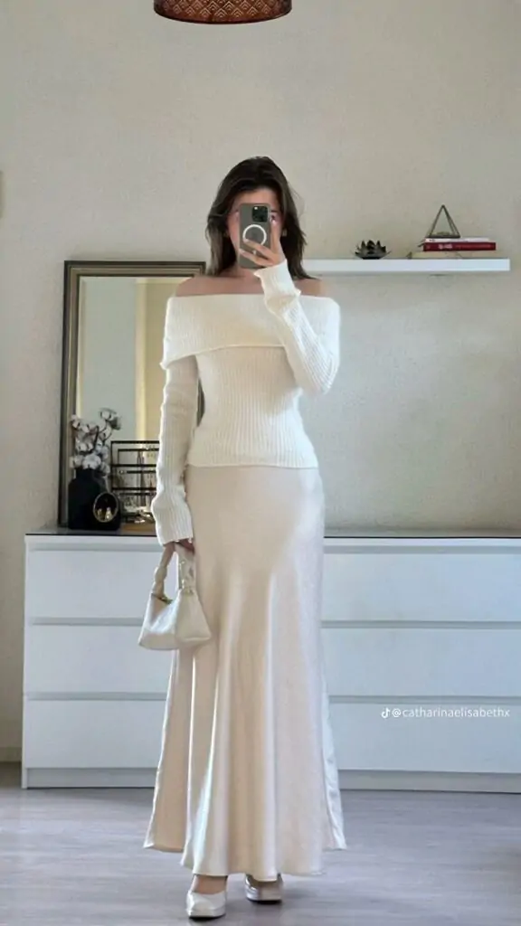 Woman in off-shoulder sweater and satin maxi skirt with a mini top-handle bag, perfect for fall.