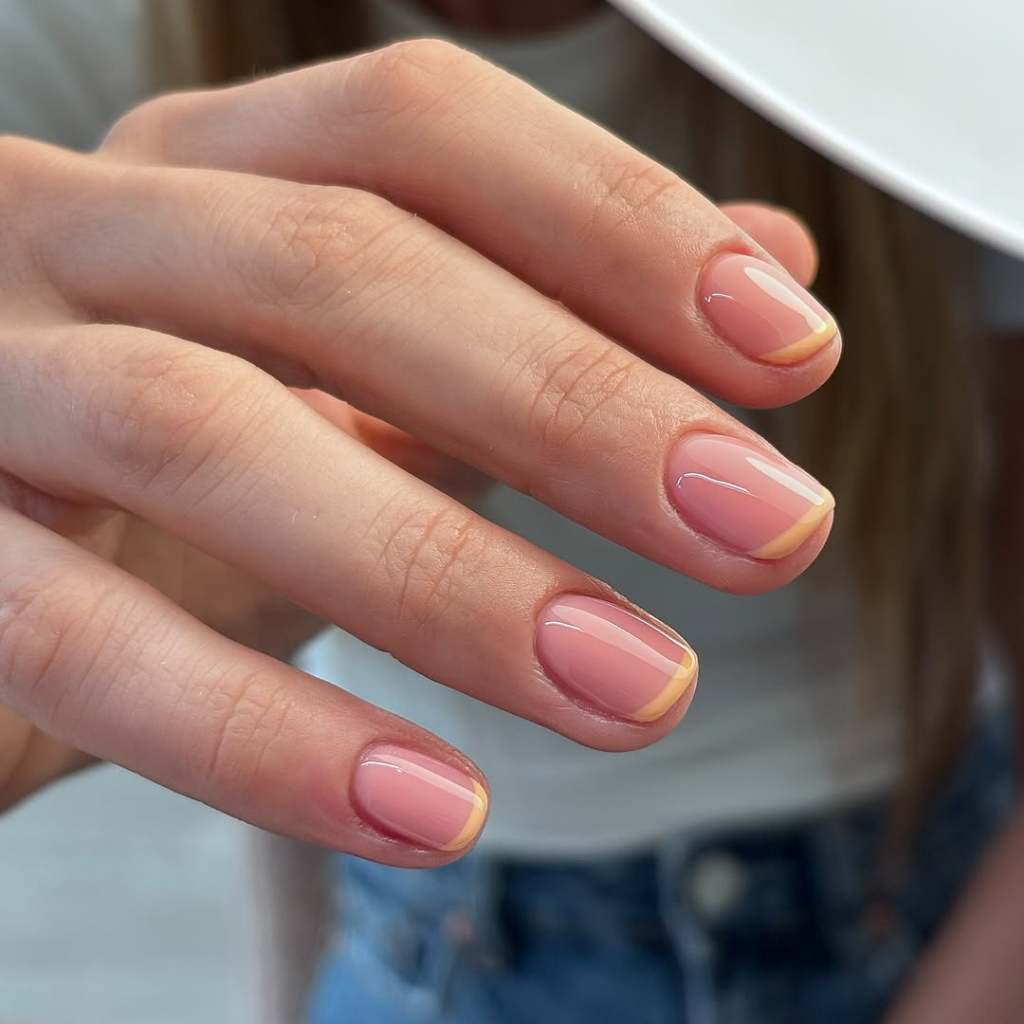 Short rounded simple nails with a warm orange micro French tip on a sheer pink base