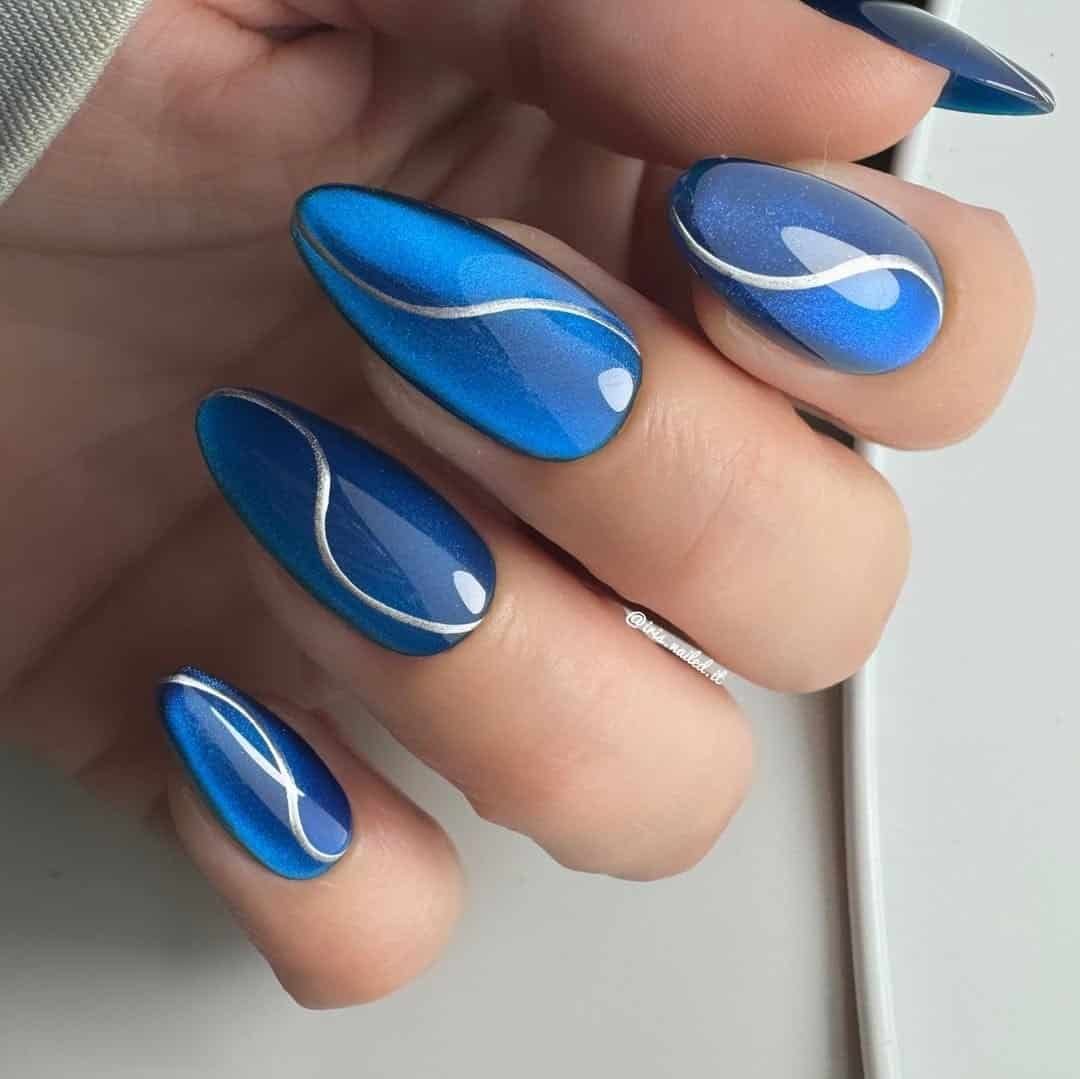 bright blue cat eye summer nails with silver wavy line art on long almond shapes.