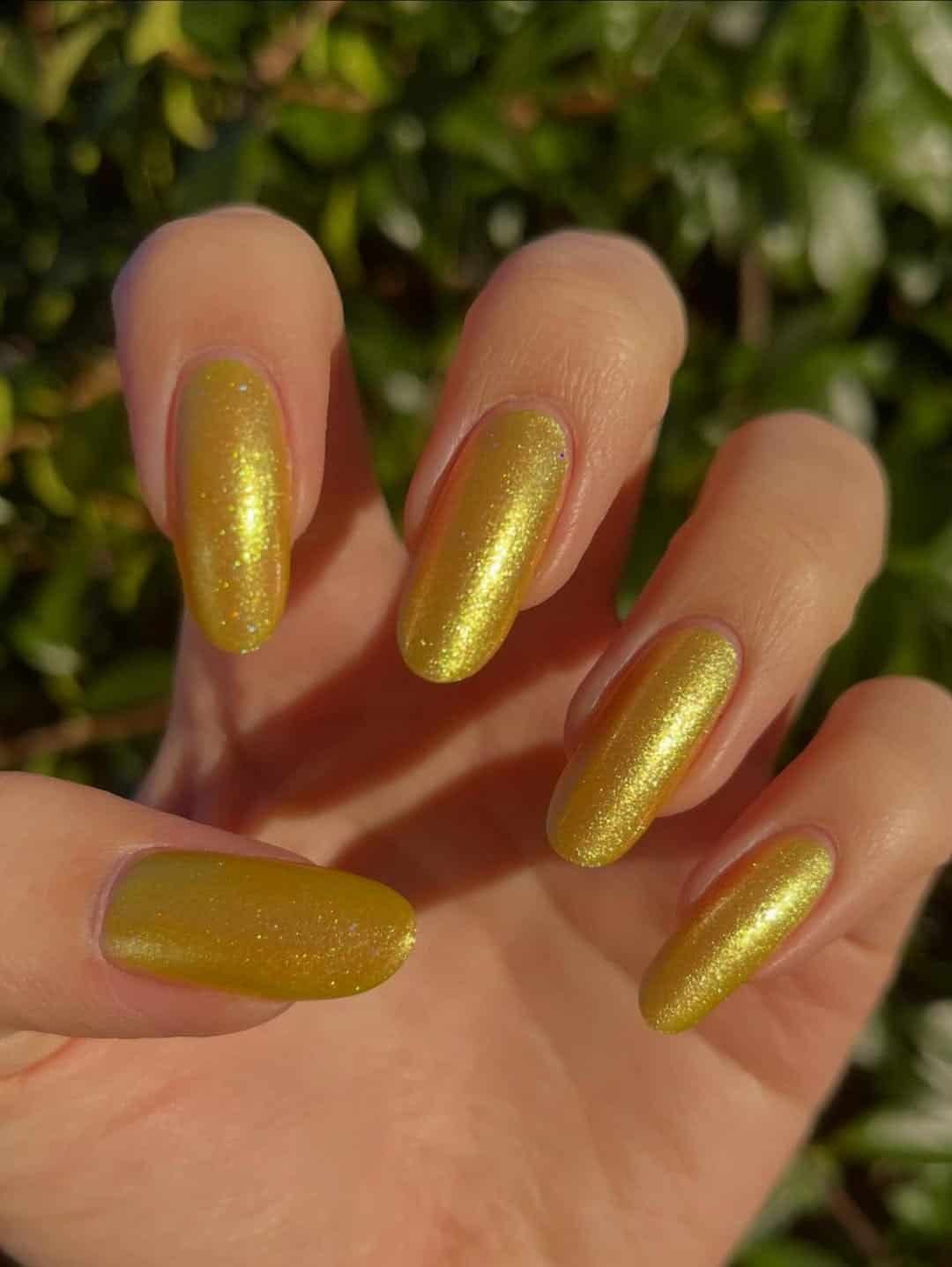 long oval nails with textured shimmery golden yellow nail polish in natural sunlight