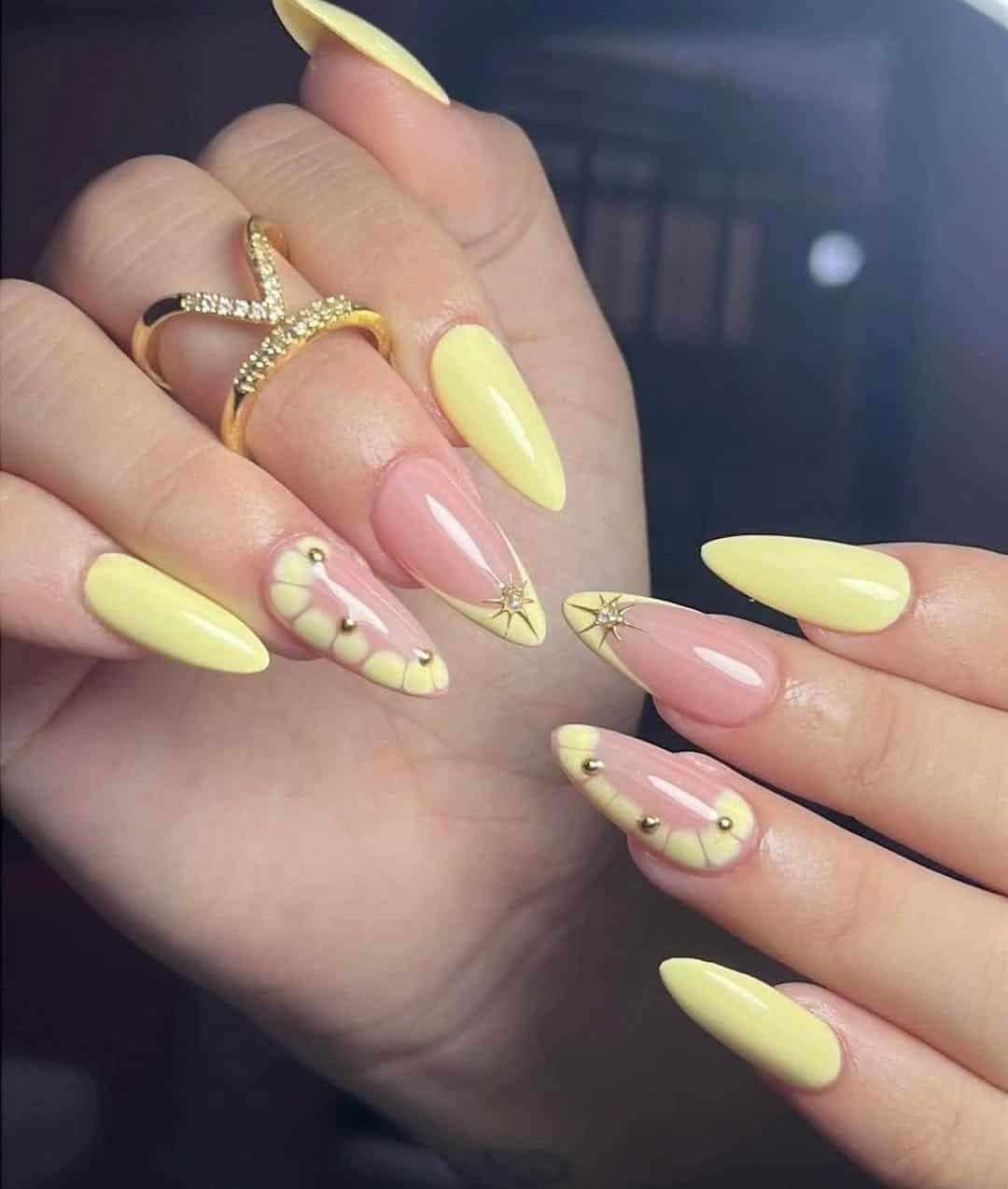 pastel yellow almond nails with french tips, gold star charms, and half moon designs