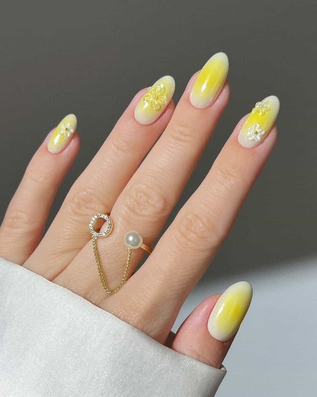 oval nails with a soft yellow aura design and 3d floral accents
