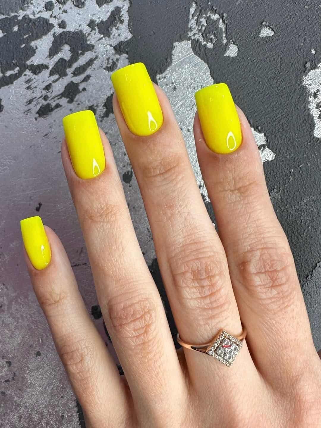vibrant neon yellow square gel nails on a hand wearing a diamond ring