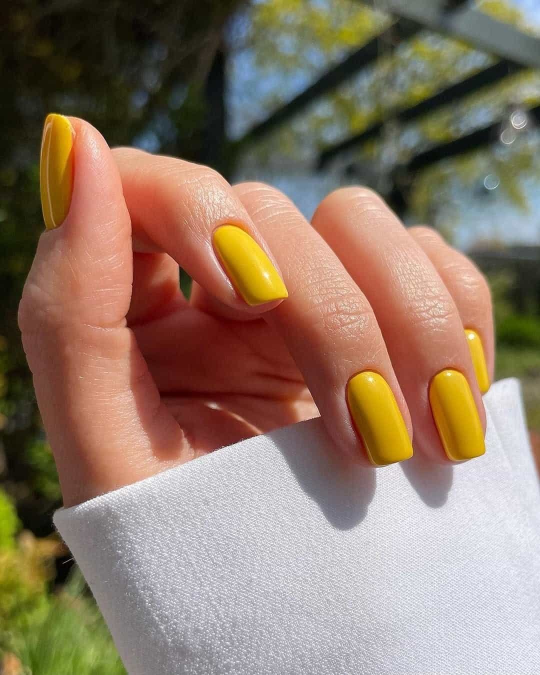 glossy bright yellow manicure on medium length square nails near a white sleeve