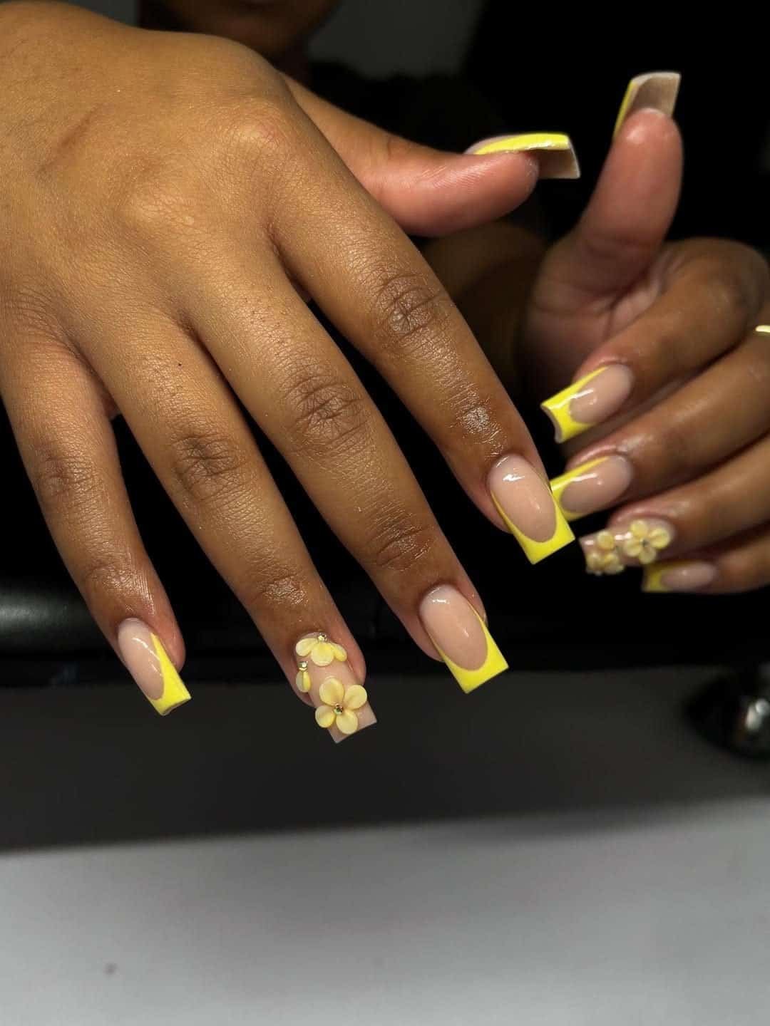 square acrylic nails with yellow french tips and three dimensional floral nail art accents